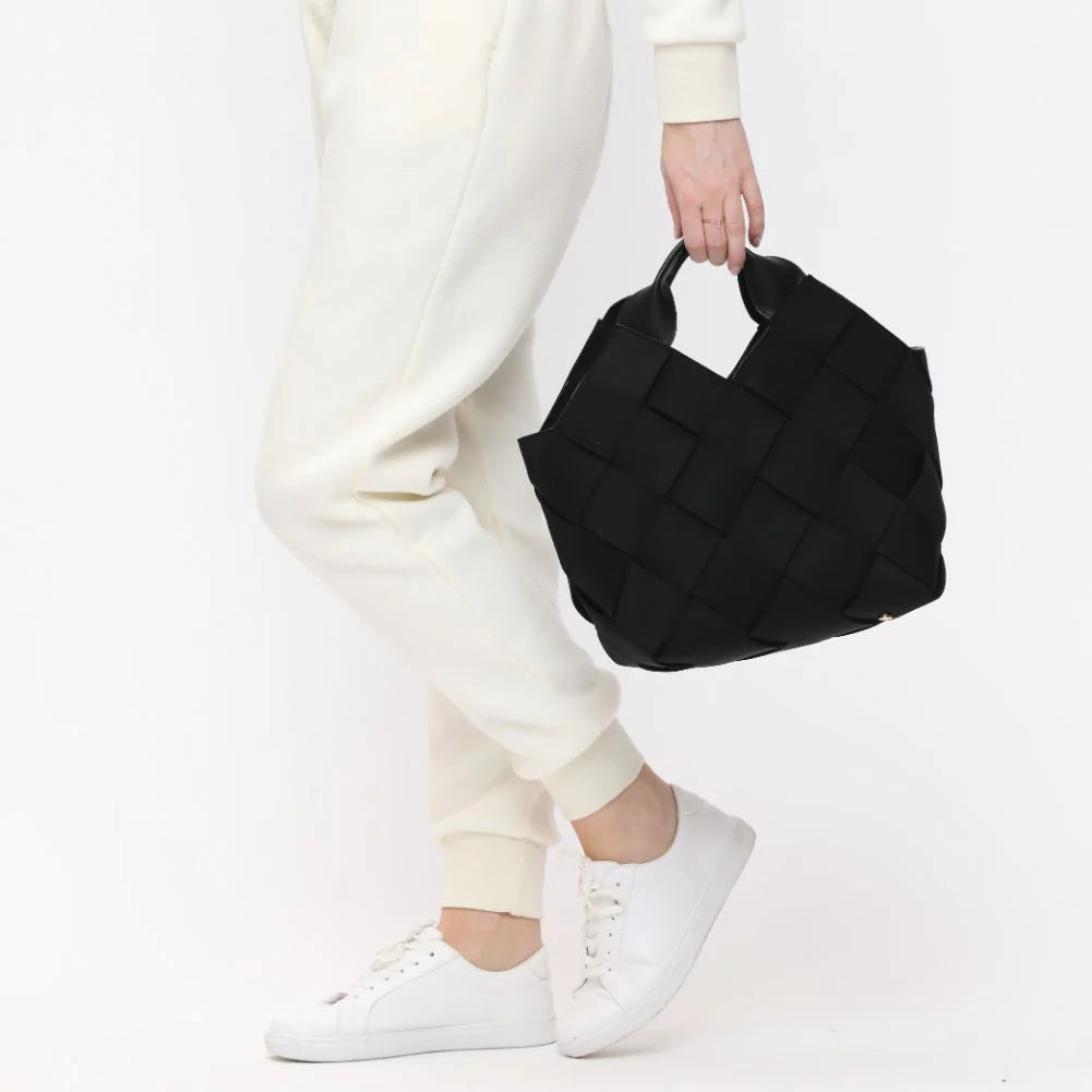 a model in sweats and sneakers carrying a black tote bag