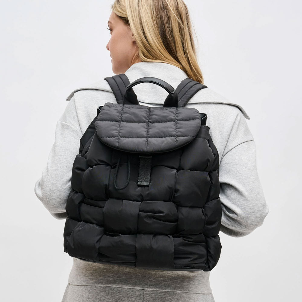 a model wearing a black quilted backpack